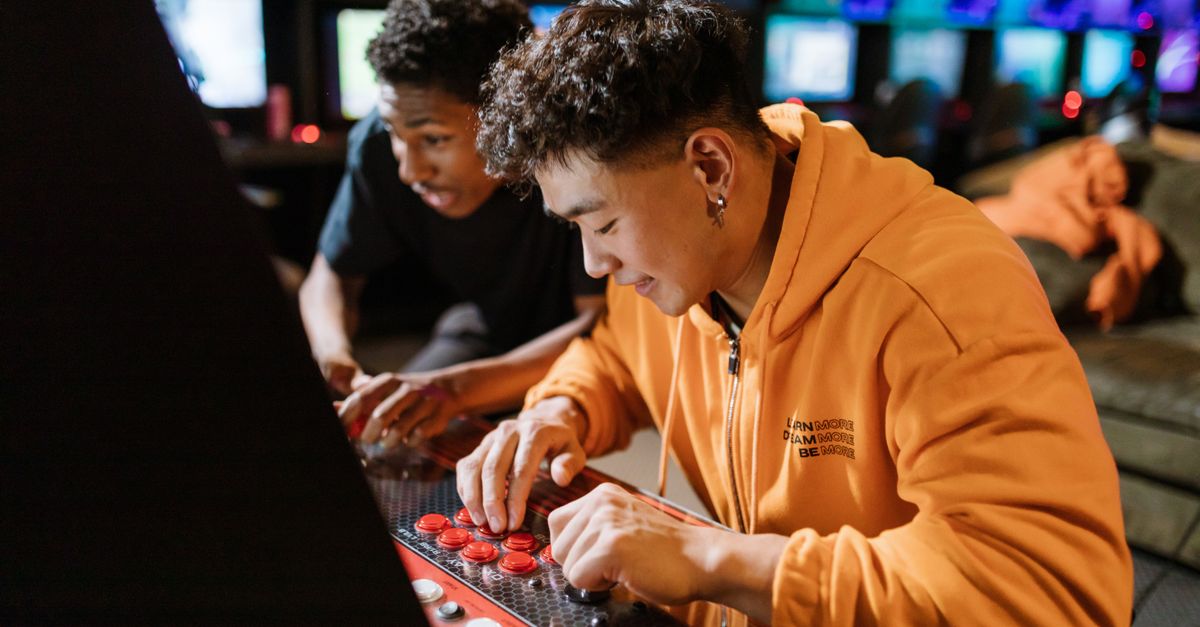Two friends enjoying a video game session on an arcade machine indoors.